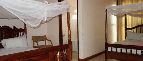 A room with two wooden beds, each with a canopy. There is a chair and a small table in the room.