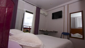 Habitación de hotel con cama, televisor en la pared, ventana con cortinas y vistas al exterior.