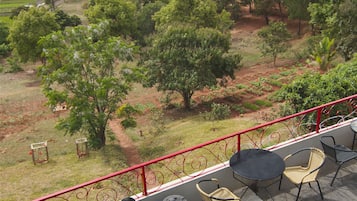 Una terrazza con posti a sedere all'aperto, ringhiera rossa e vista su un paesaggio rurale con alberi e campi.