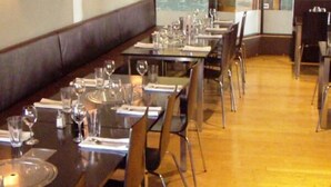 Un restaurante con mesas largas, sillas y piso de madera.
