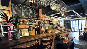 Zona de bar con mostrador de madera, taburetes y un menú en una pizarra.
