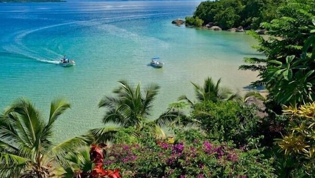 Una playa tropical con aguas turquesas cristalinas, embarcaciones y exuberante follaje.