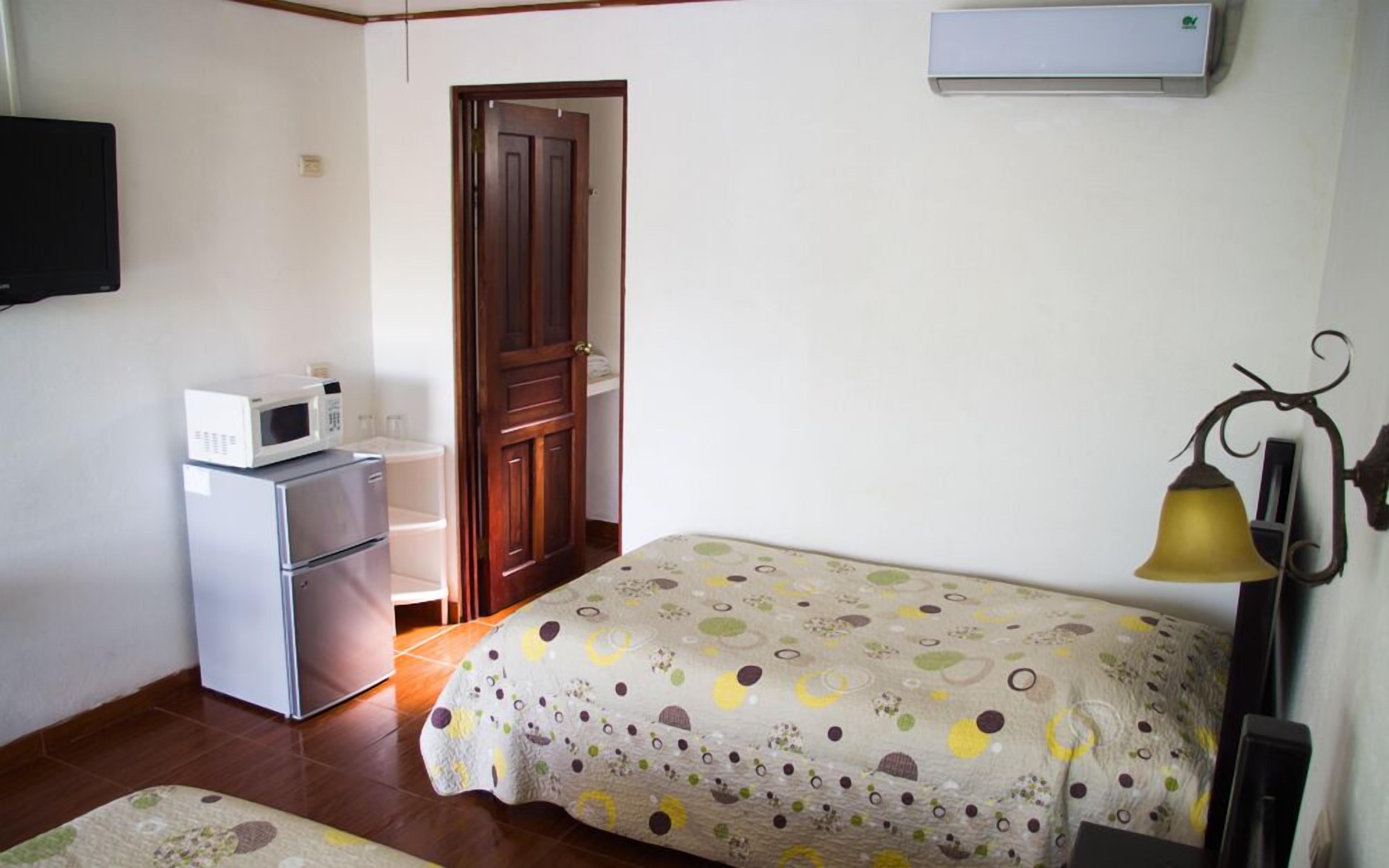 Una habitación pequeña con una cama, un microondas, un refrigerador, una puerta y un aire acondicionado instalado en la pared.