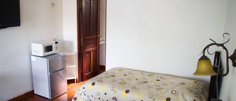 Una habitación pequeña con una cama, un microondas, un refrigerador, una puerta y un aire acondicionado instalado en la pared.