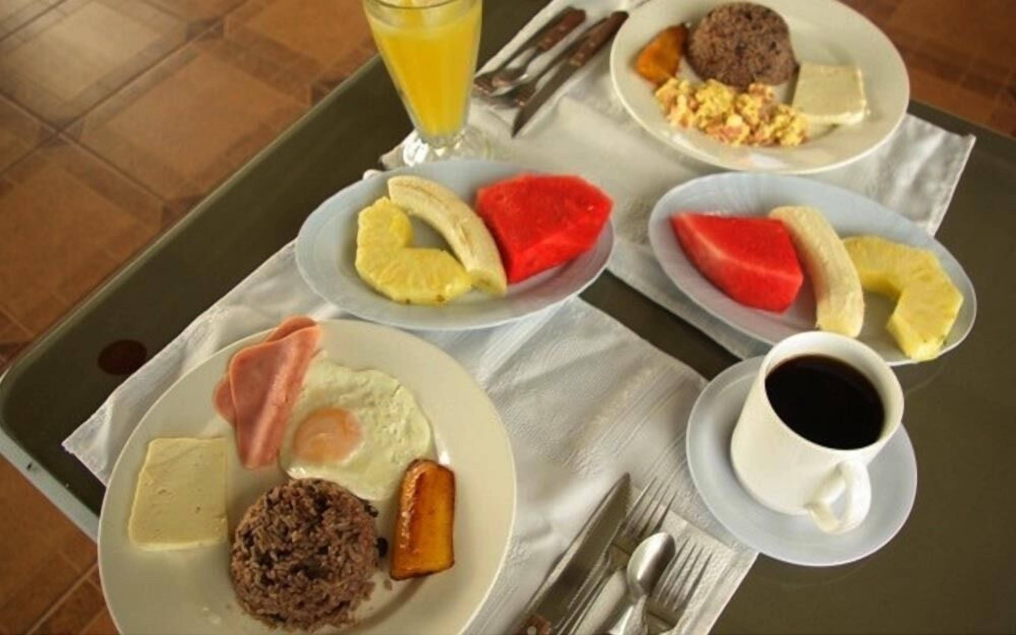 A breakfast tray with eggs, bacon, toast, and fruit, along with a cup of coffee and a glass of orange juice.