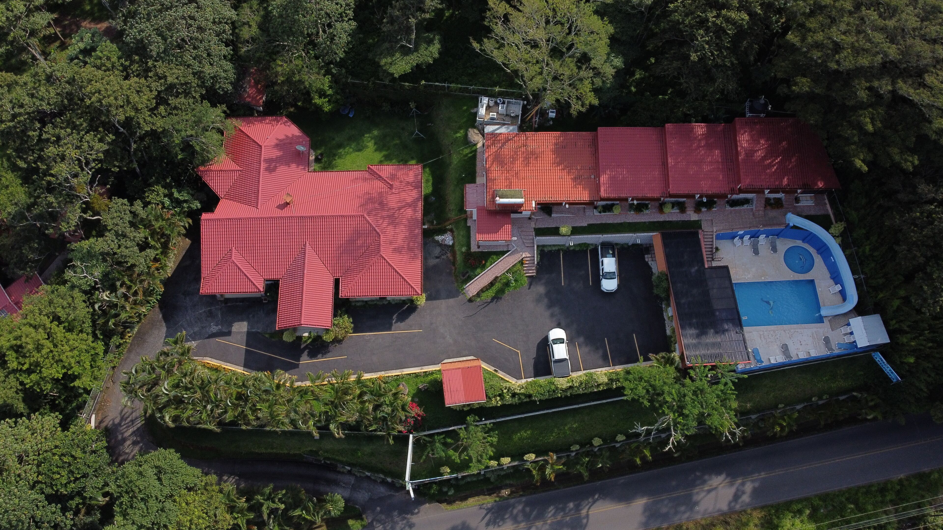 An aerial view of a property with a large red-roofed building, a swimming pool, and a parking area.