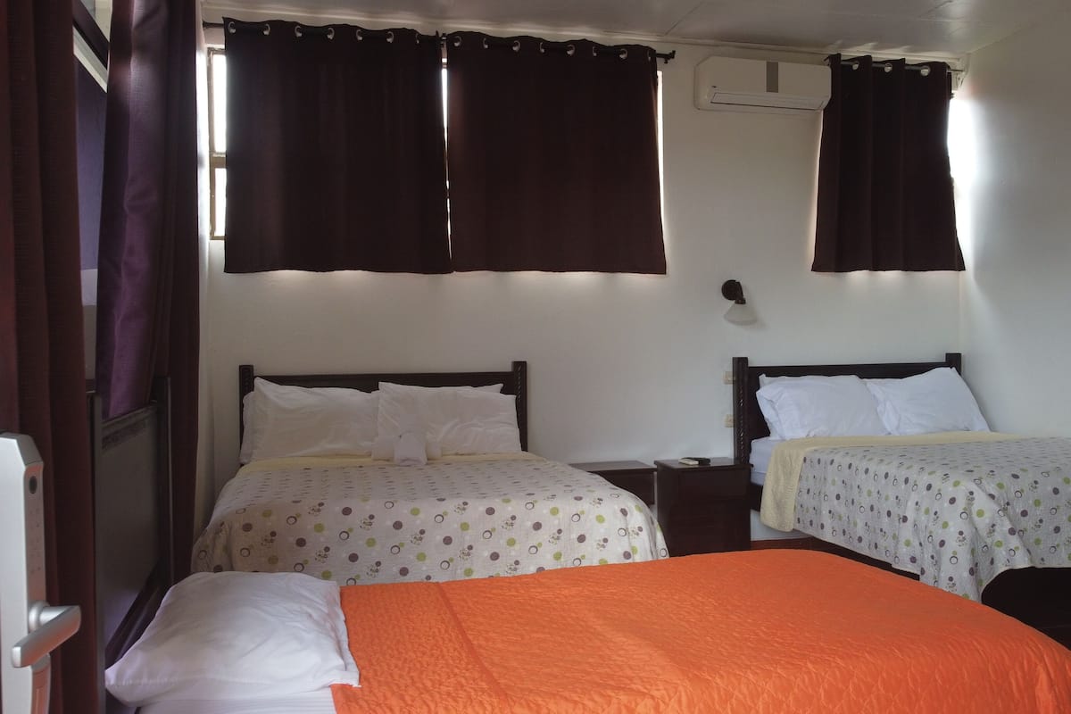 A hotel room with two beds, a window with curtains, an air conditioning unit, and a bedside lamp.