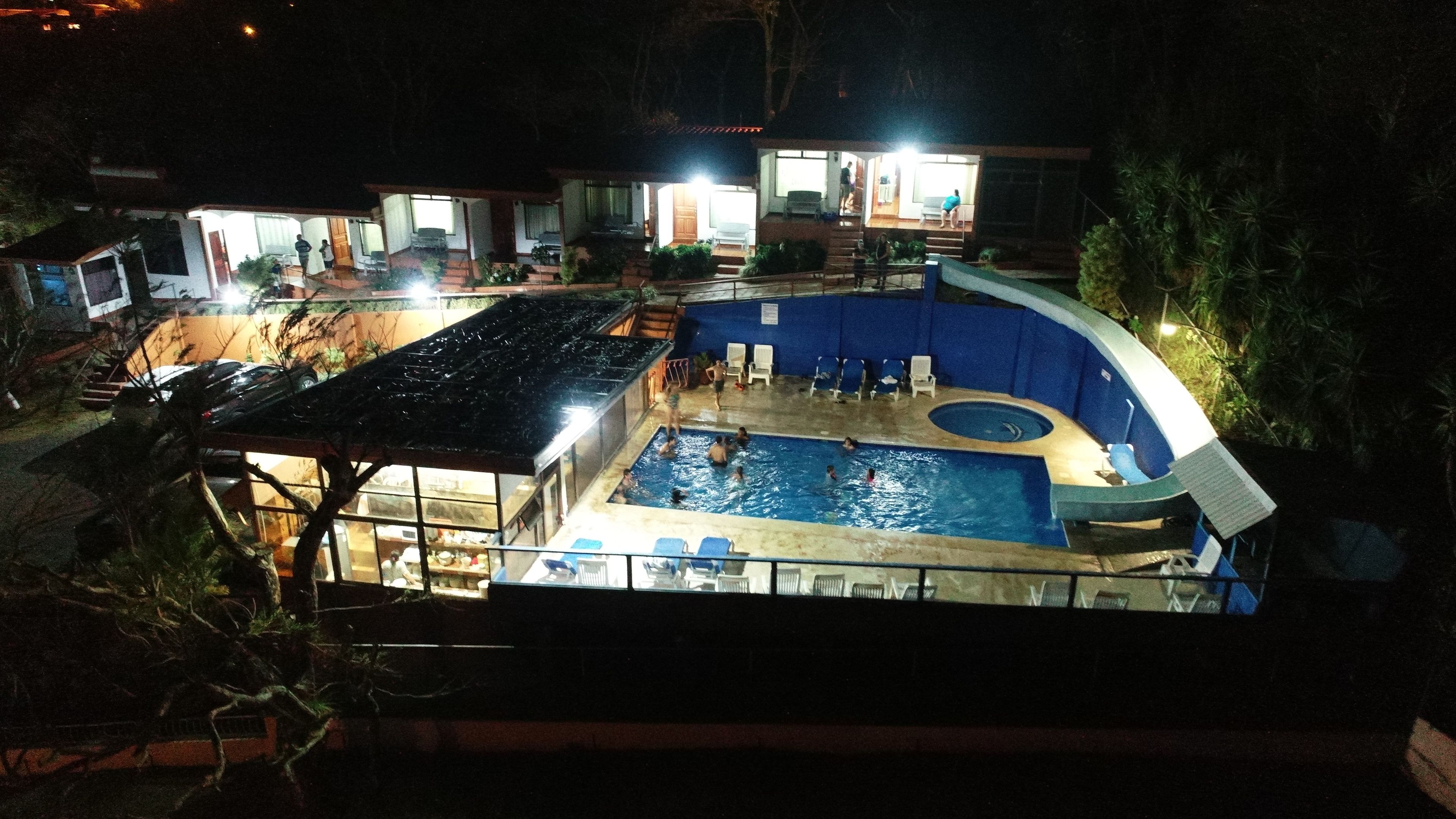A swimming pool with a hot tub, surrounded by lounge chairs and a covered area with tables and chairs.