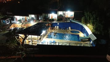 A swimming pool with a hot tub, surrounded by lounge chairs and a covered area with tables and chairs.