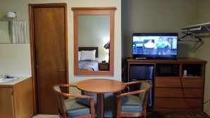 Une chambre d’hôtel avec une porte en bois, un lit recouvert d’une courtepointe colorée, une petite table ronde avec deux chaises, un téléviseur posé sur un meuble en bois et un miroir accroché au mur.