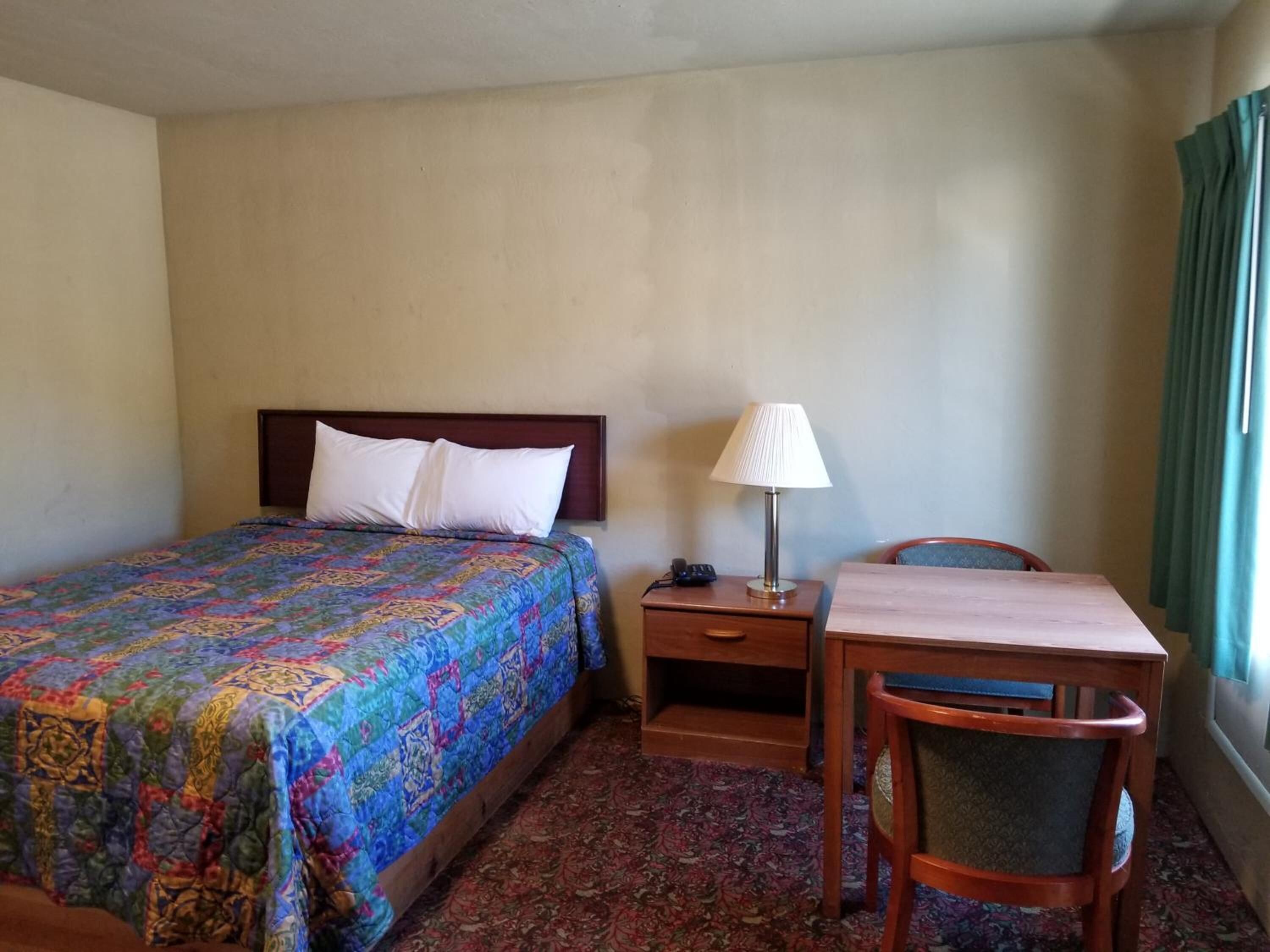 Une chambre d’hôtel avec un lit, une table de chevet avec une lampe, une chaise et un petit bureau.