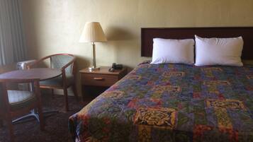 Habitación de hotel con una cama, dos almohadas, una mesita de noche con lámpara, una silla y una pequeña mesa.