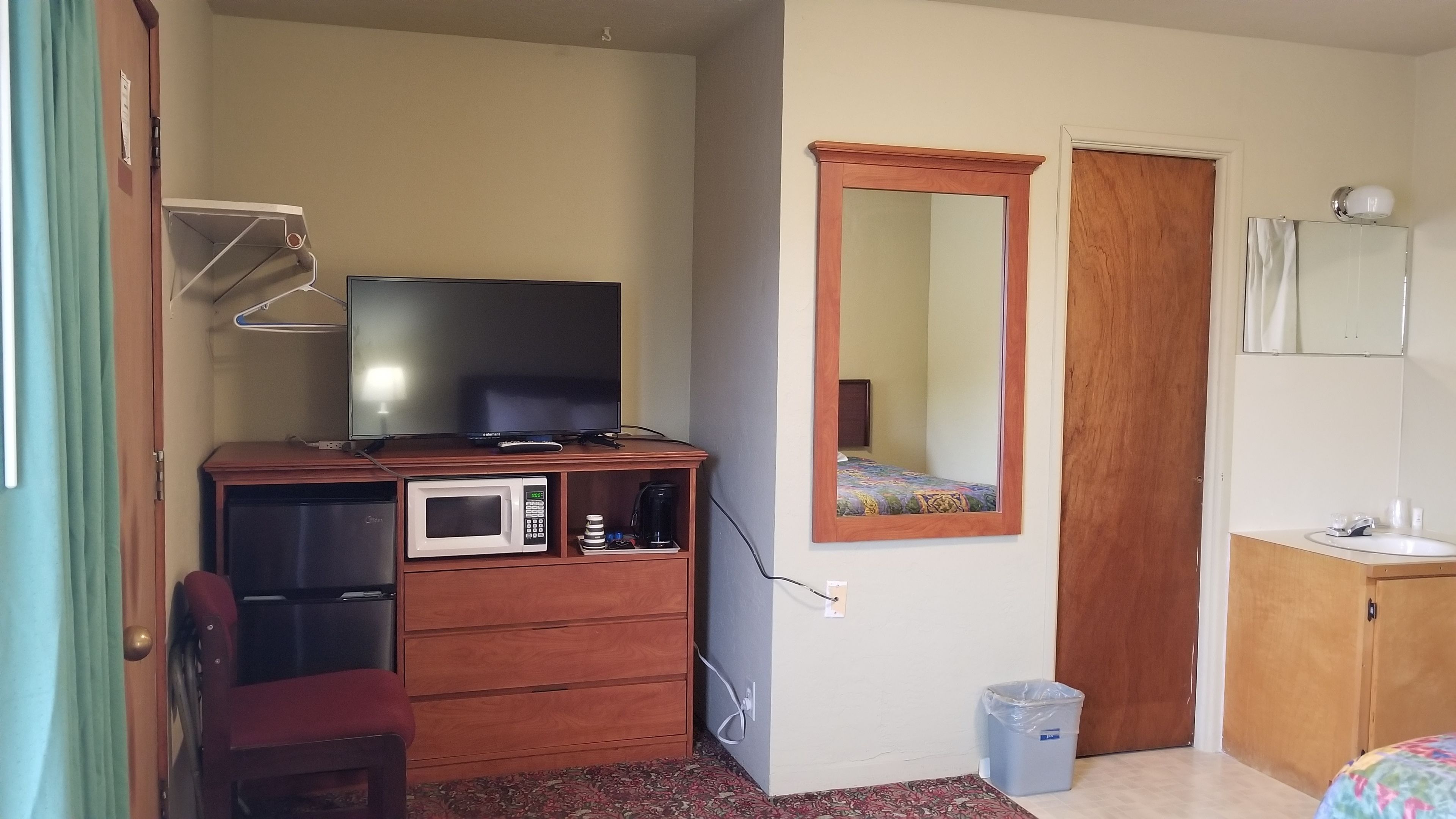 Habitación de hotel con televisión, microondas, mueble pequeño, espejo, cama y puerta.