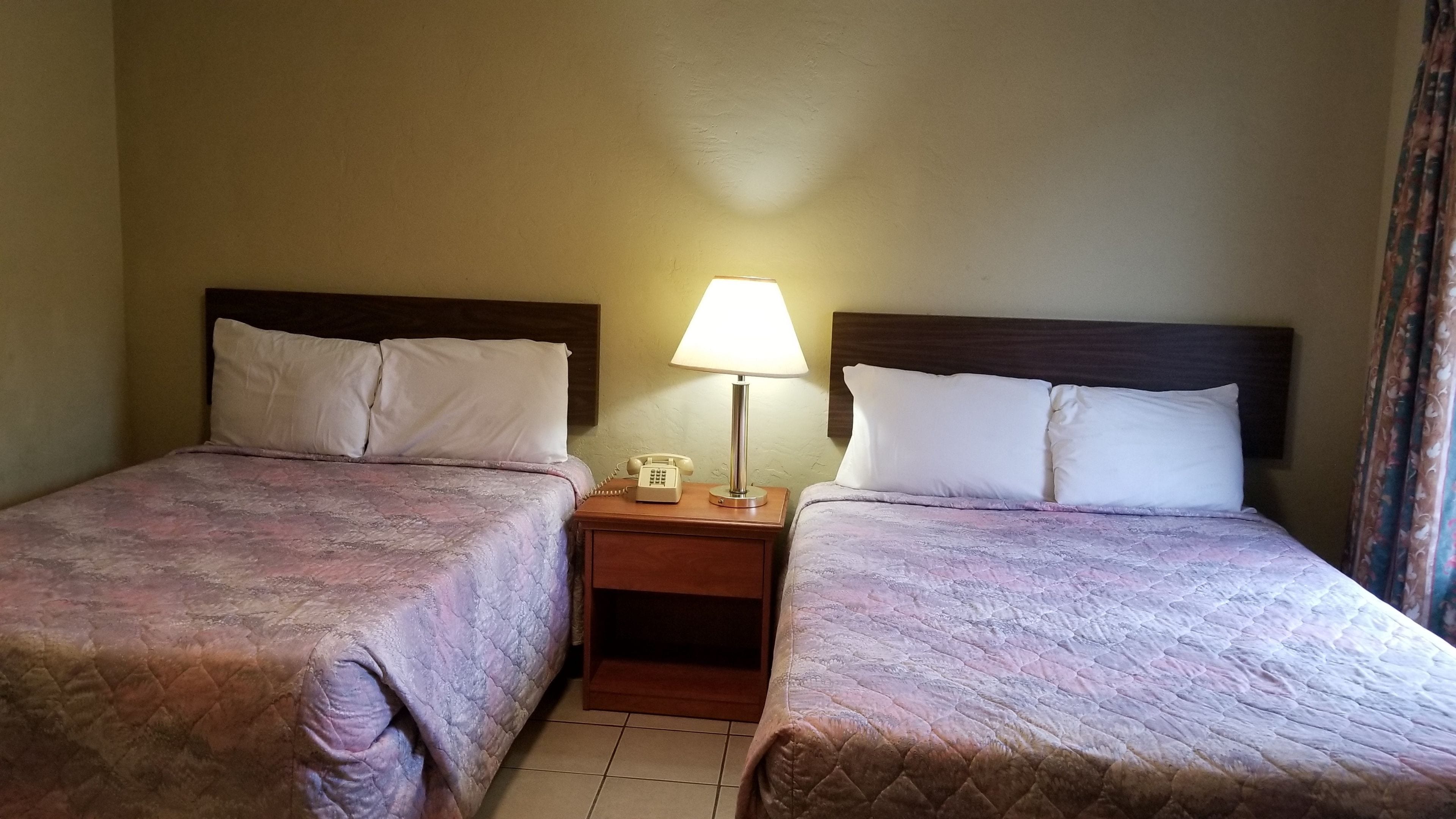 A hotel room with two beds, each with a headboard, a bedside table with a lamp, and a telephone.