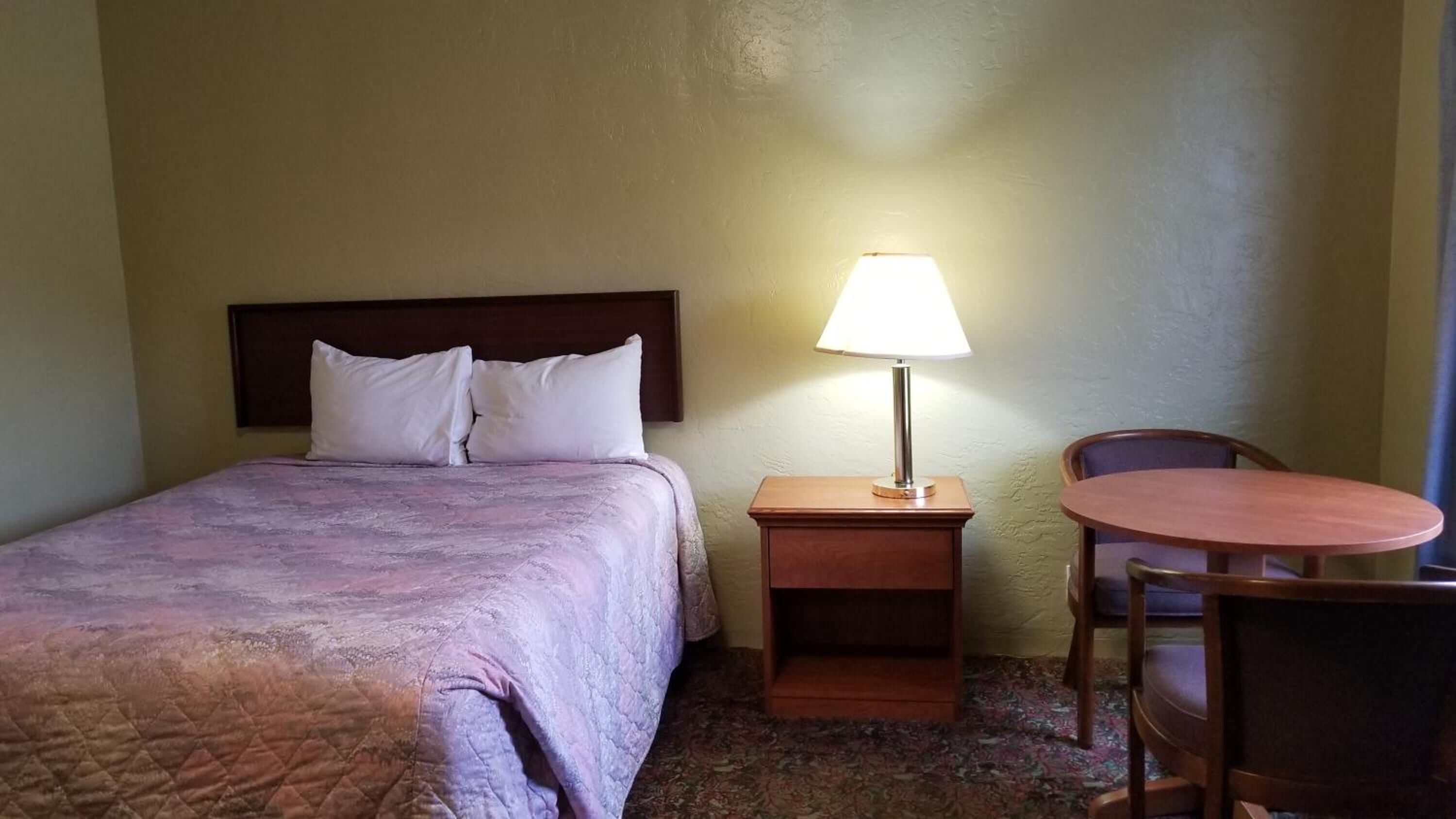 Une chambre d’hôtel comprenant un lit, une table de chevet avec une lampe, une chaise et une petite table.