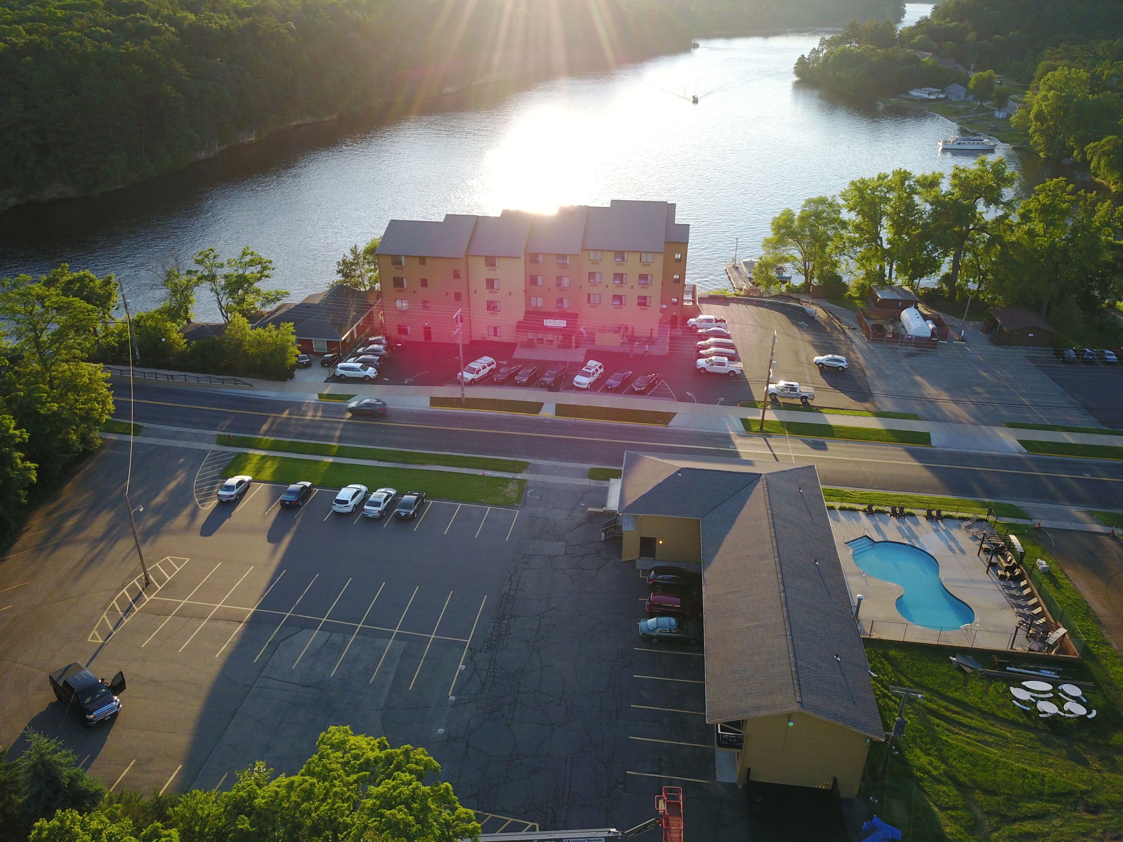 An aerial view of a hotel with a parking lot, swimming pool, and a river in the background.