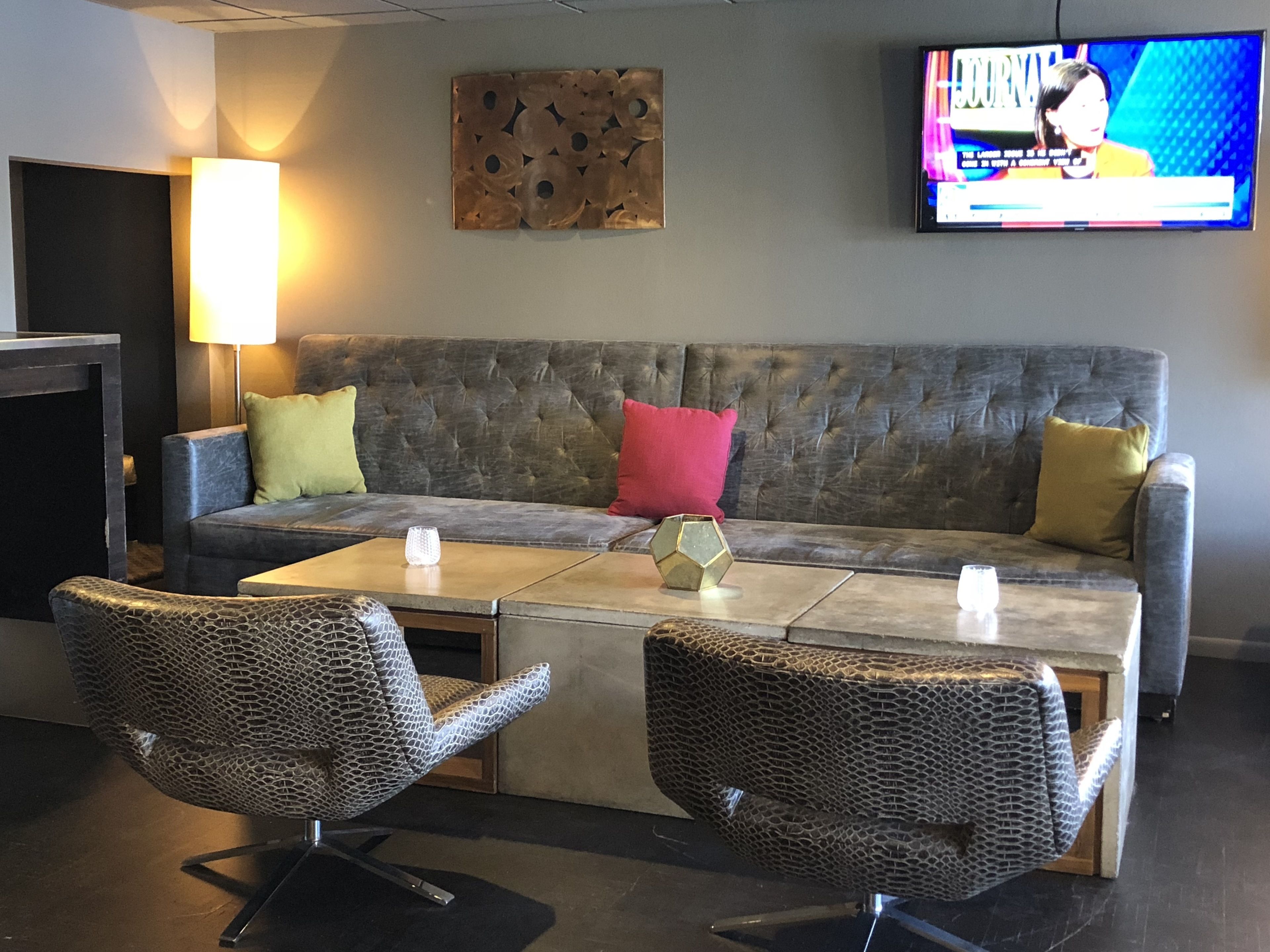 Uma sala de estar moderna com um sofá cinza estofado, duas poltronas estampadas, uma mesa de centro e uma TV de tela plana fixada na parede.
