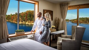 A room with large windows overlooking a lake, a bed, a desk, and a chair.
