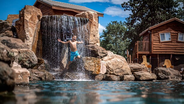 A wooden cabin with a waterfall feature and a pool.