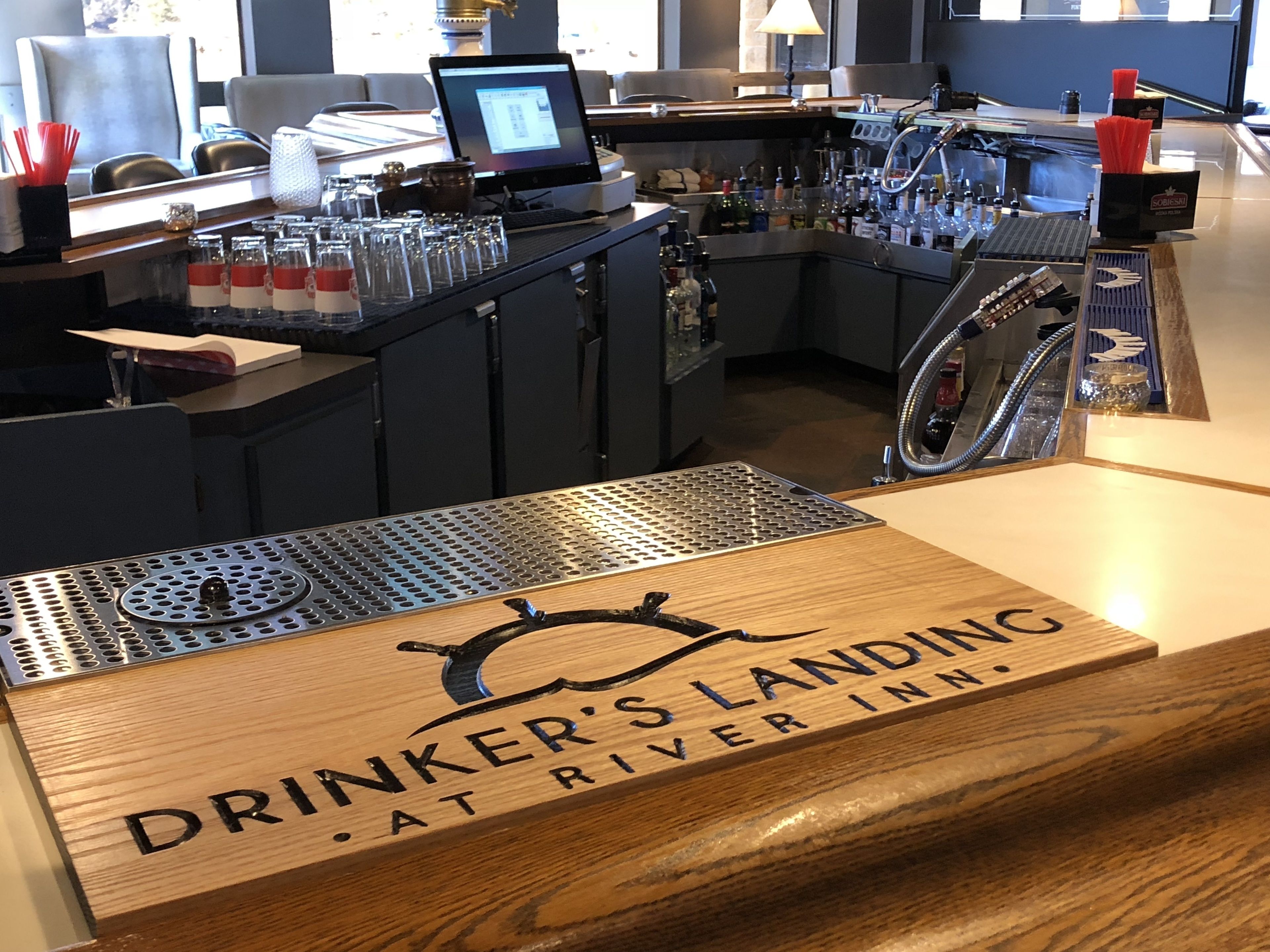 Zona de bar con mostrador de madera que muestra 'DRINKER'S LANDING AT RIVER INN'.