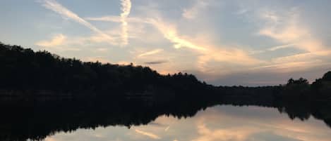 Ein ruhiger See spiegelt den Himmel mit Wolken und einen bewaldeten Hang.
