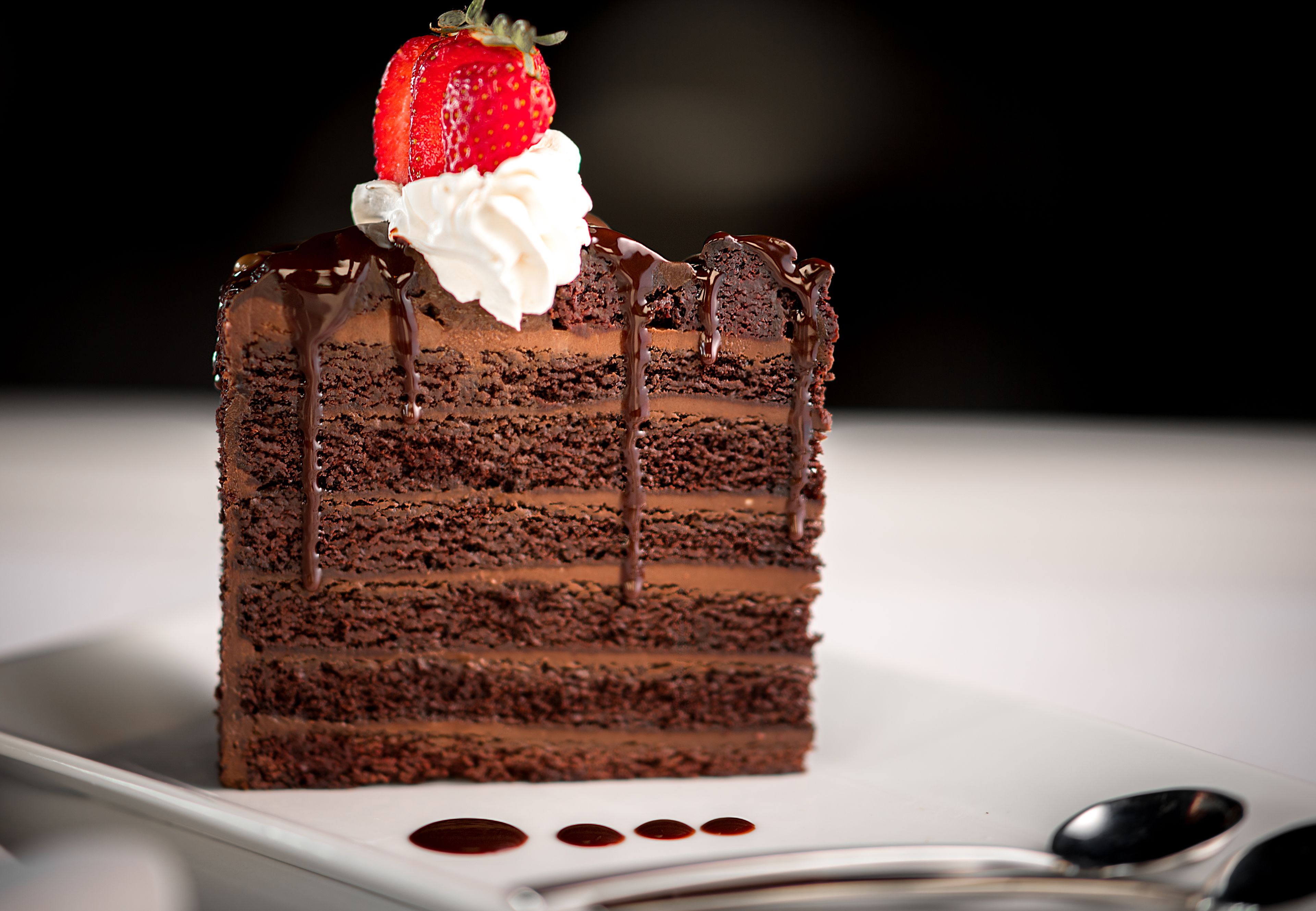 Une part de gâteau au chocolat à plusieurs couches, surmontée d’une fraise et nappée de crème fouettée.