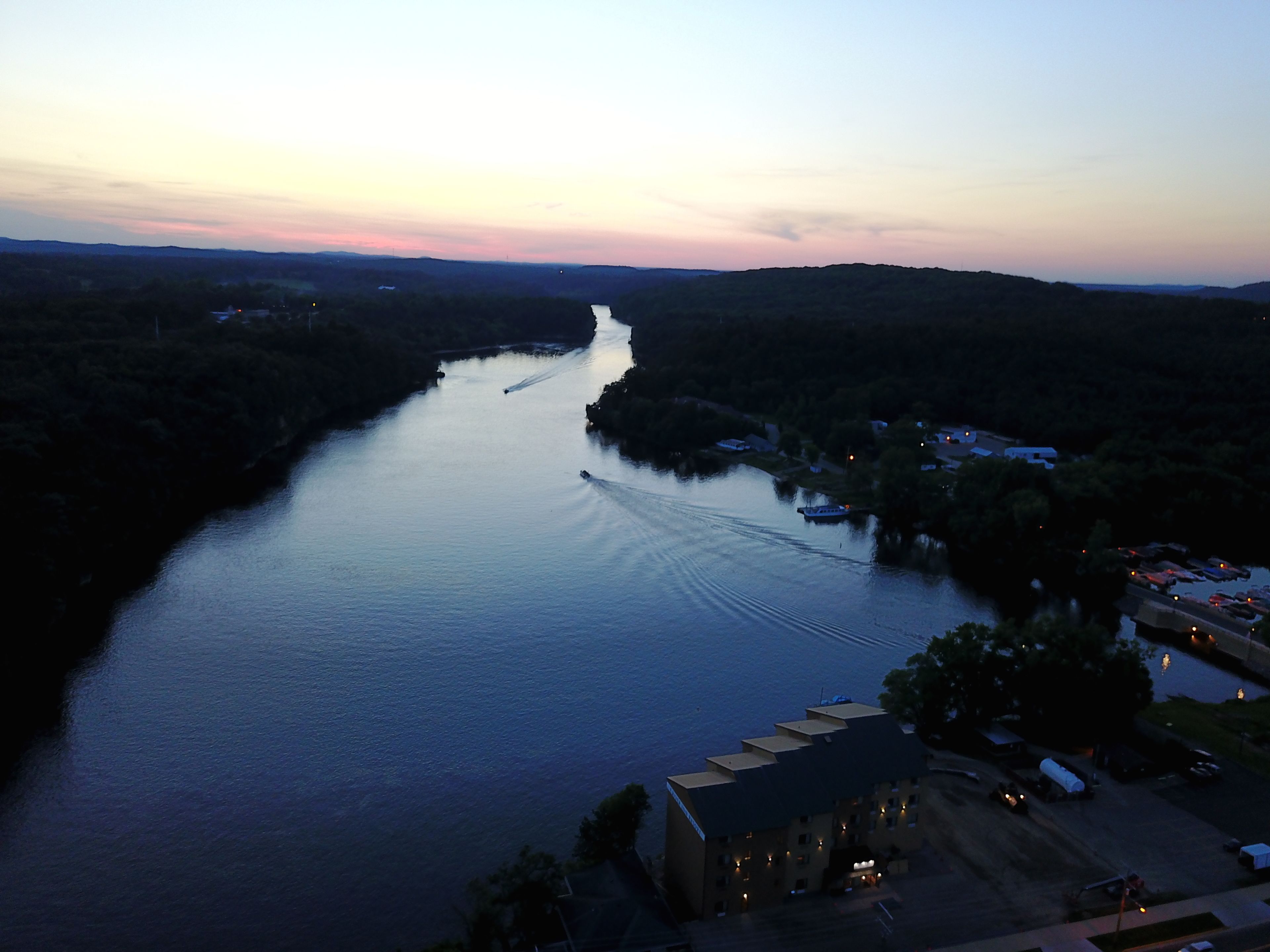 A river with boats, surrounded by hills and a building with multiple windows.