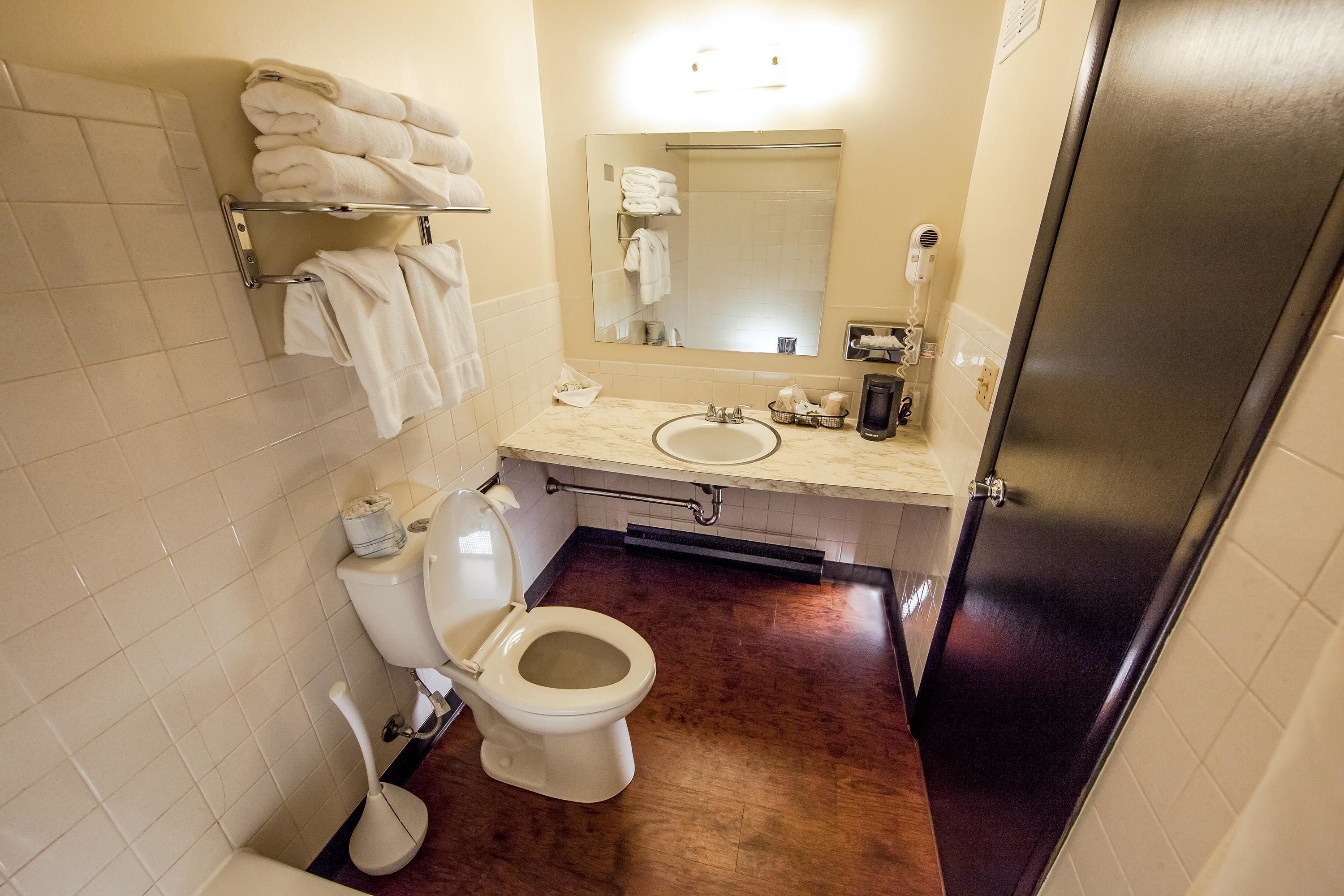 Une salle de bain comprenant des toilettes, un lavabo, un miroir, un porte-serviettes et un espace douche.