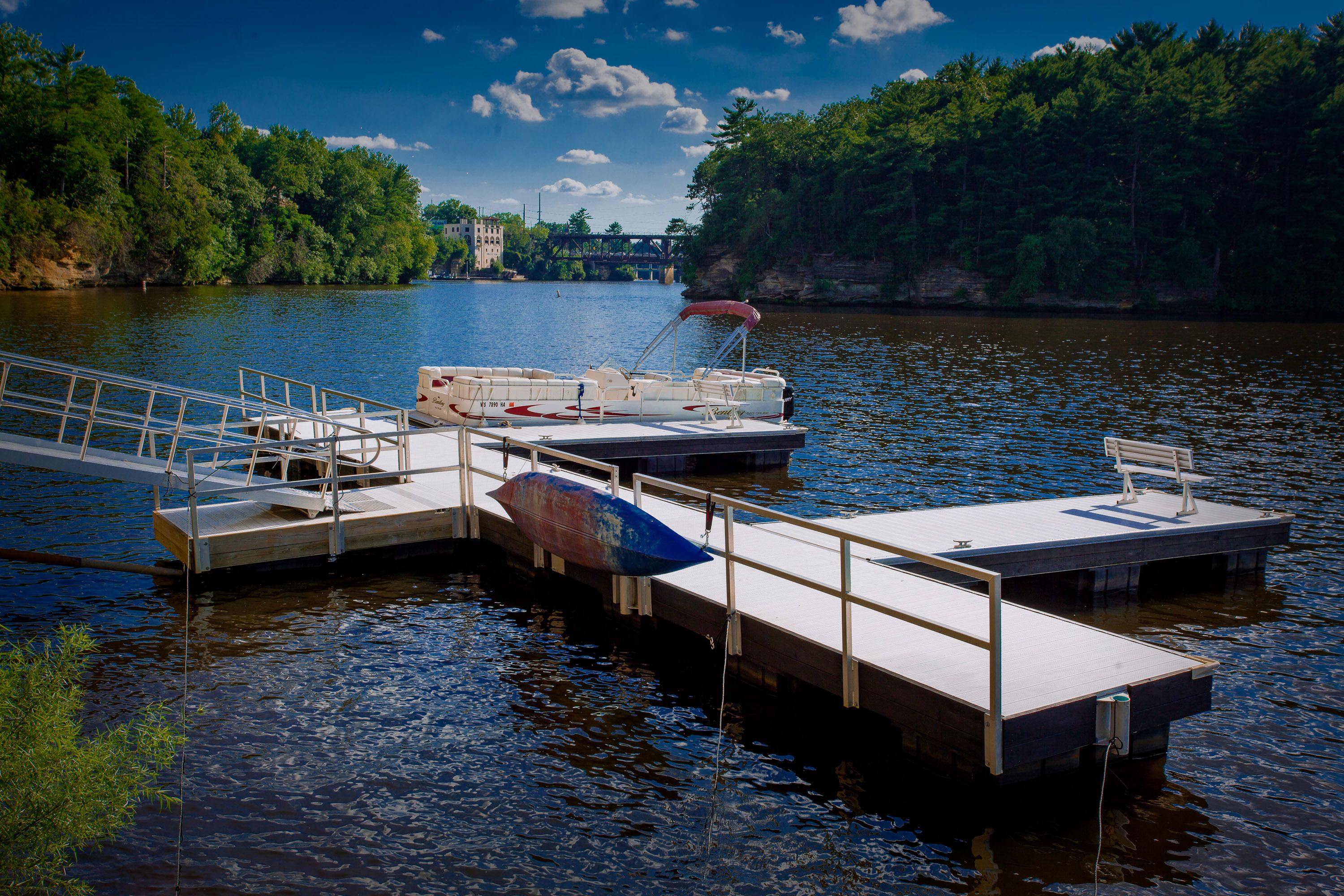 A dock with boats, a wooden walkway, and a bridge in the background.