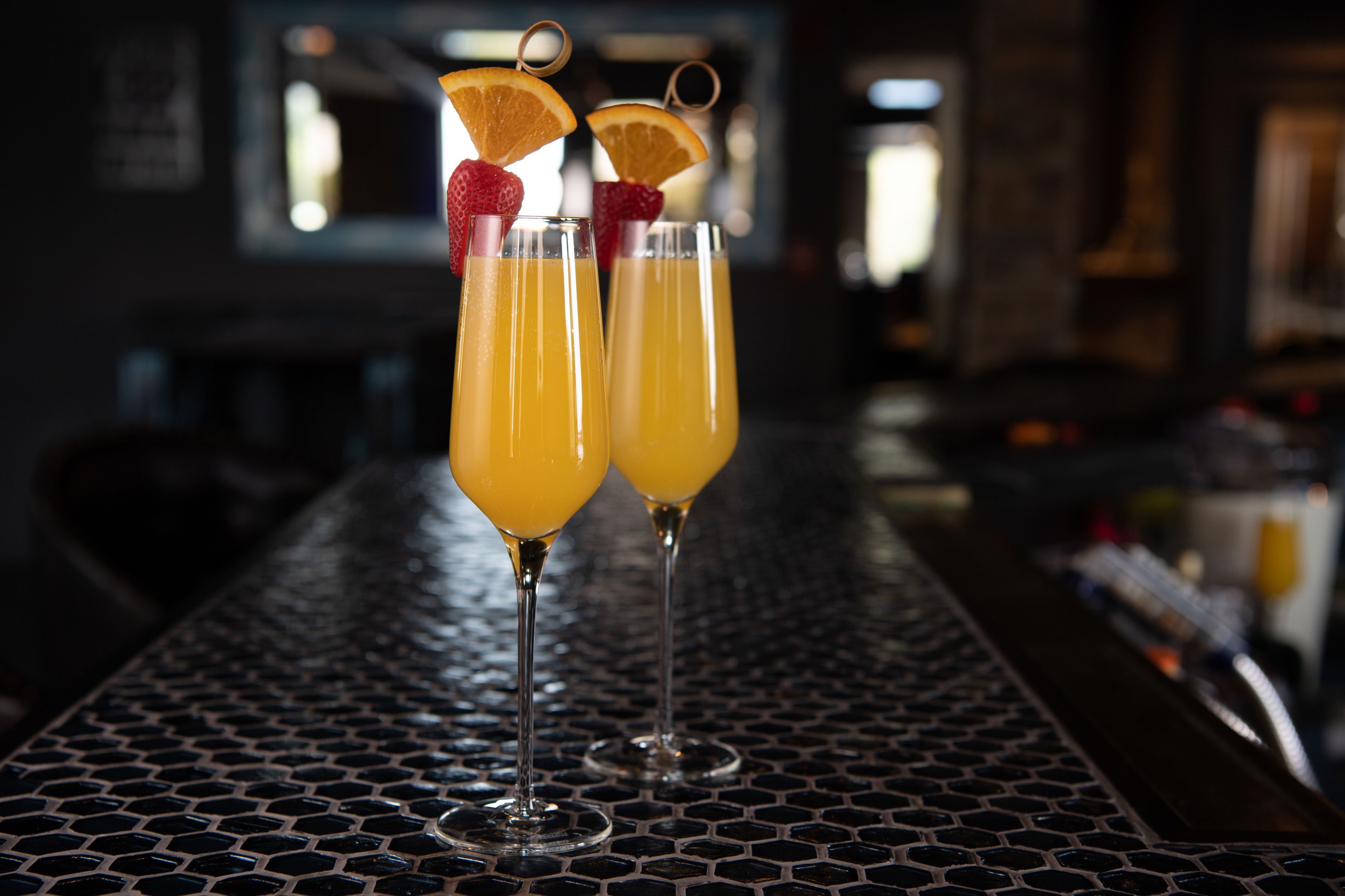 Two glasses of orange juice on a metal bar counter with a hexagonal pattern.