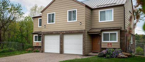 A two-story house with a garage, a brick foundation, and a gravel driveway.