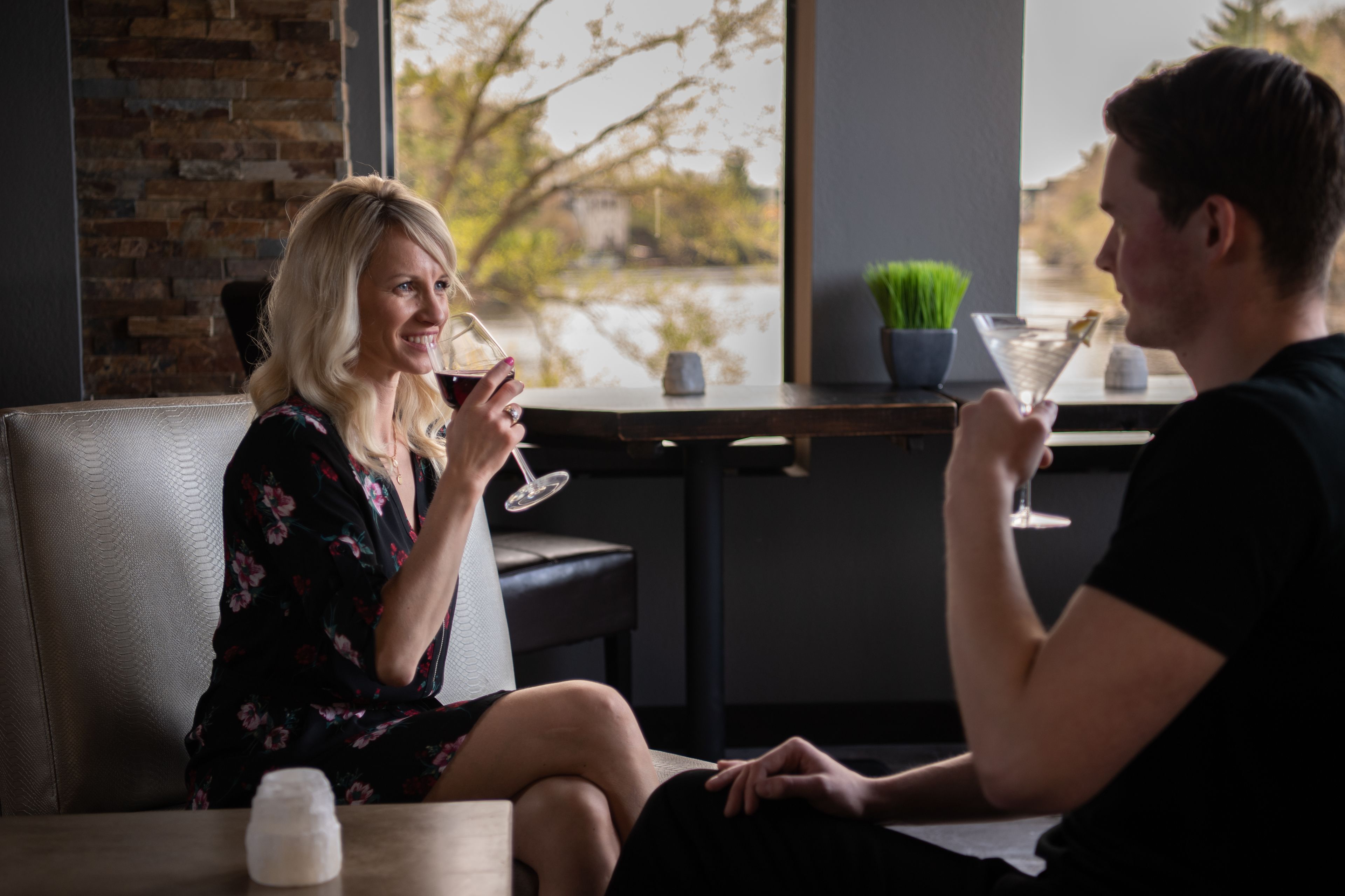 Una pareja sentada en una mesa de restaurante con vista a un muro de ladrillo y una ventana que da a la calle.