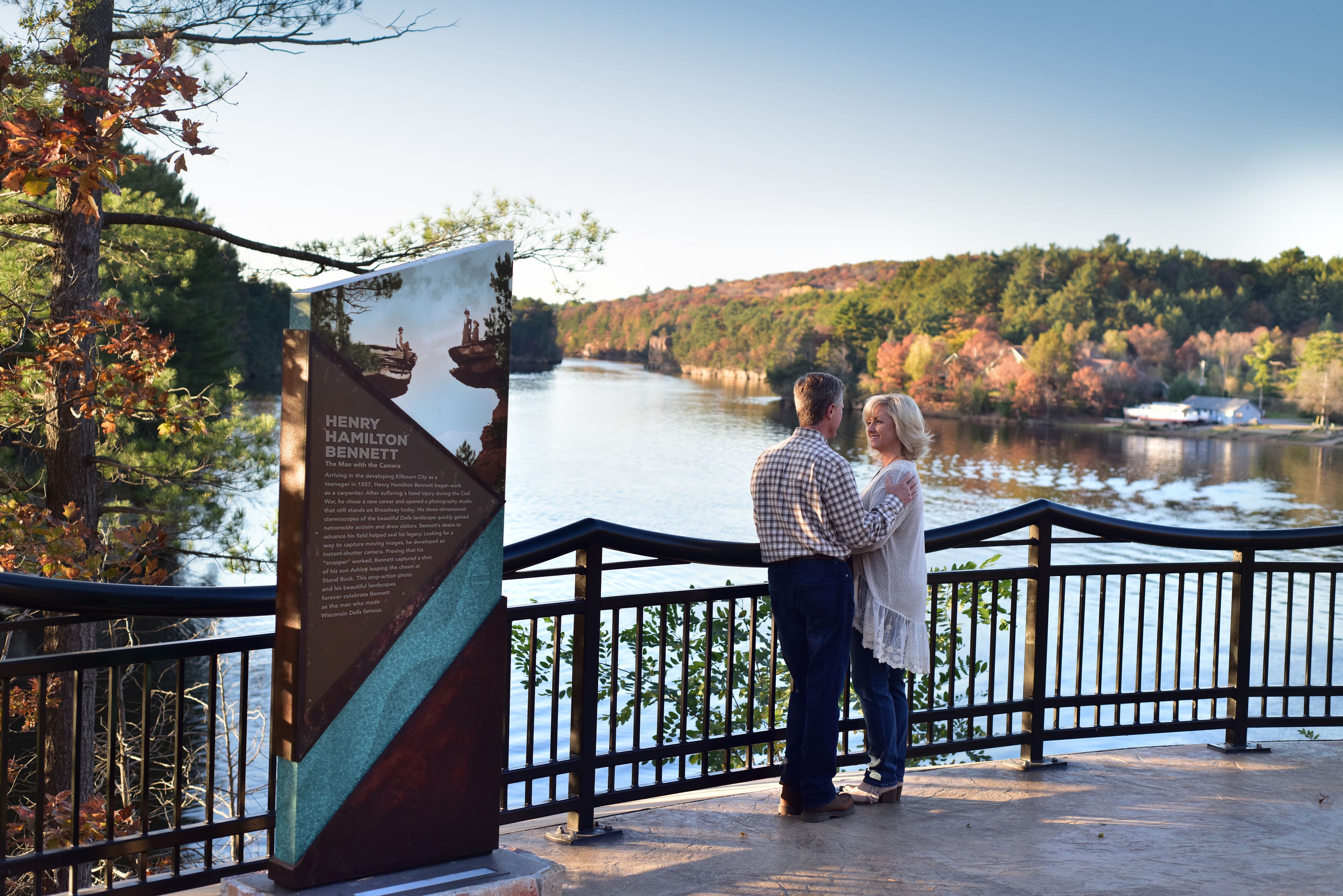 A couple standing by a lake with a historical marker in the foreground.