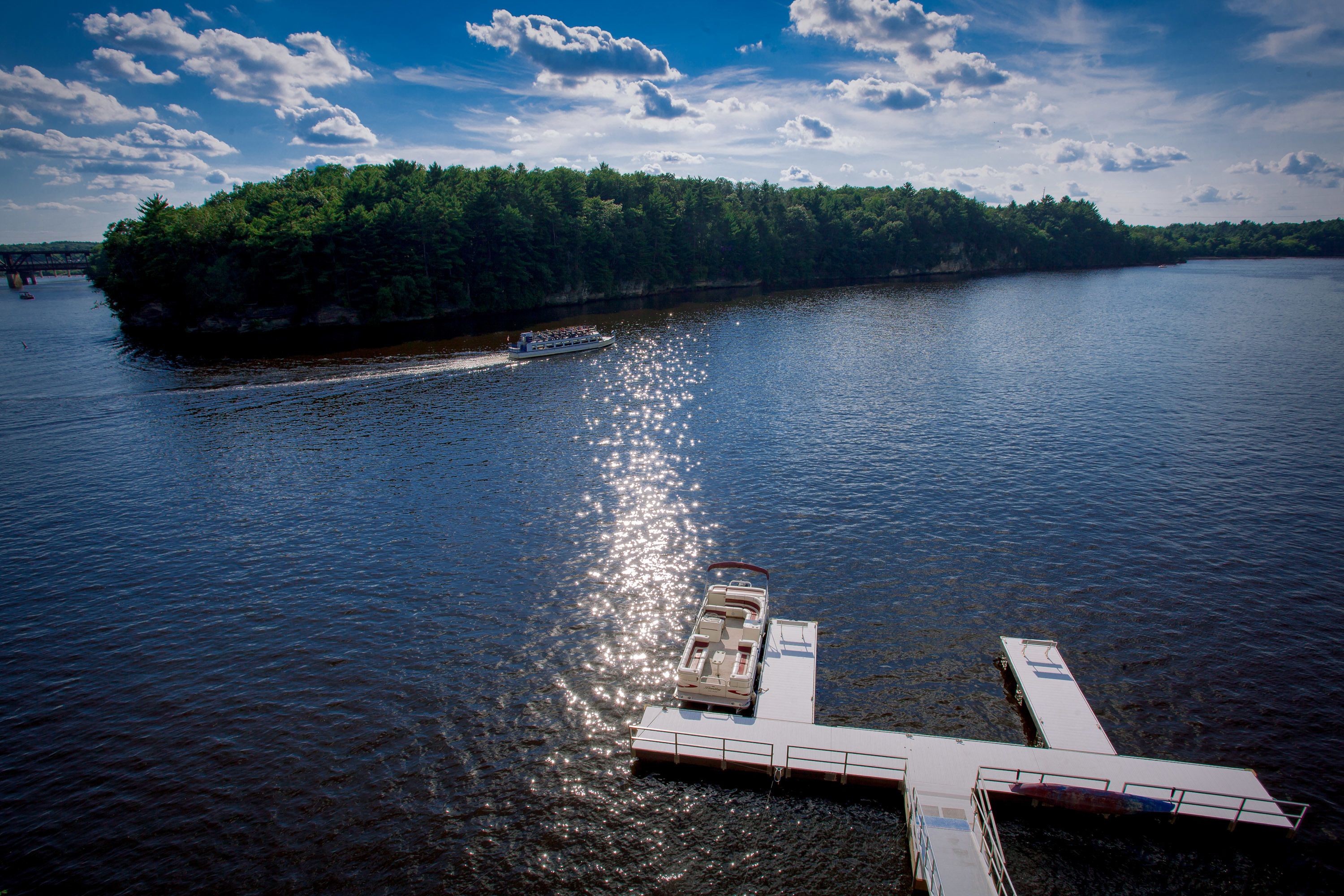 A boat docked at a pier with a forested island in the background.