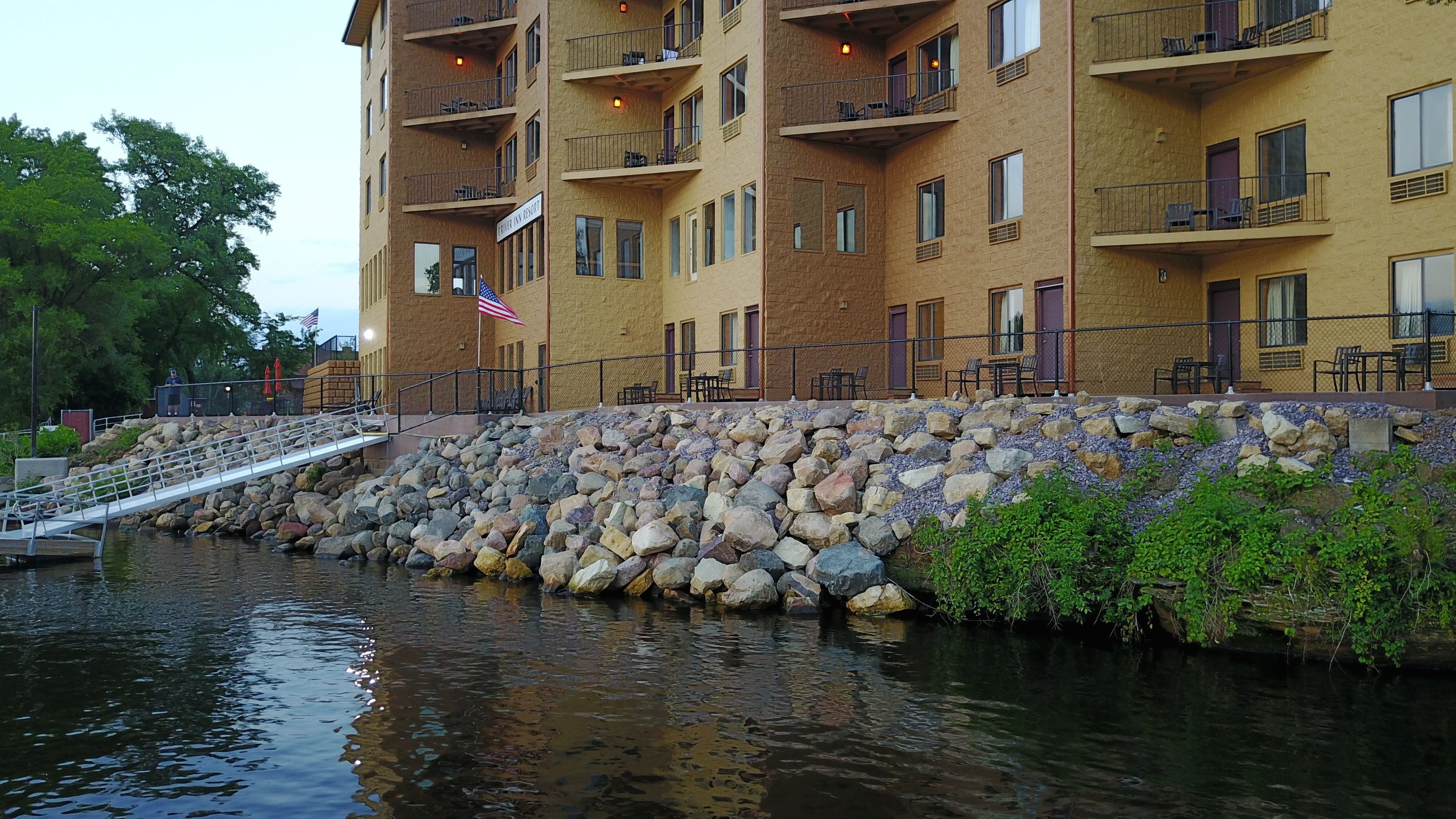 A multi-story hotel with balconies, a stone retaining wall, and a small bridge over a body of water.
