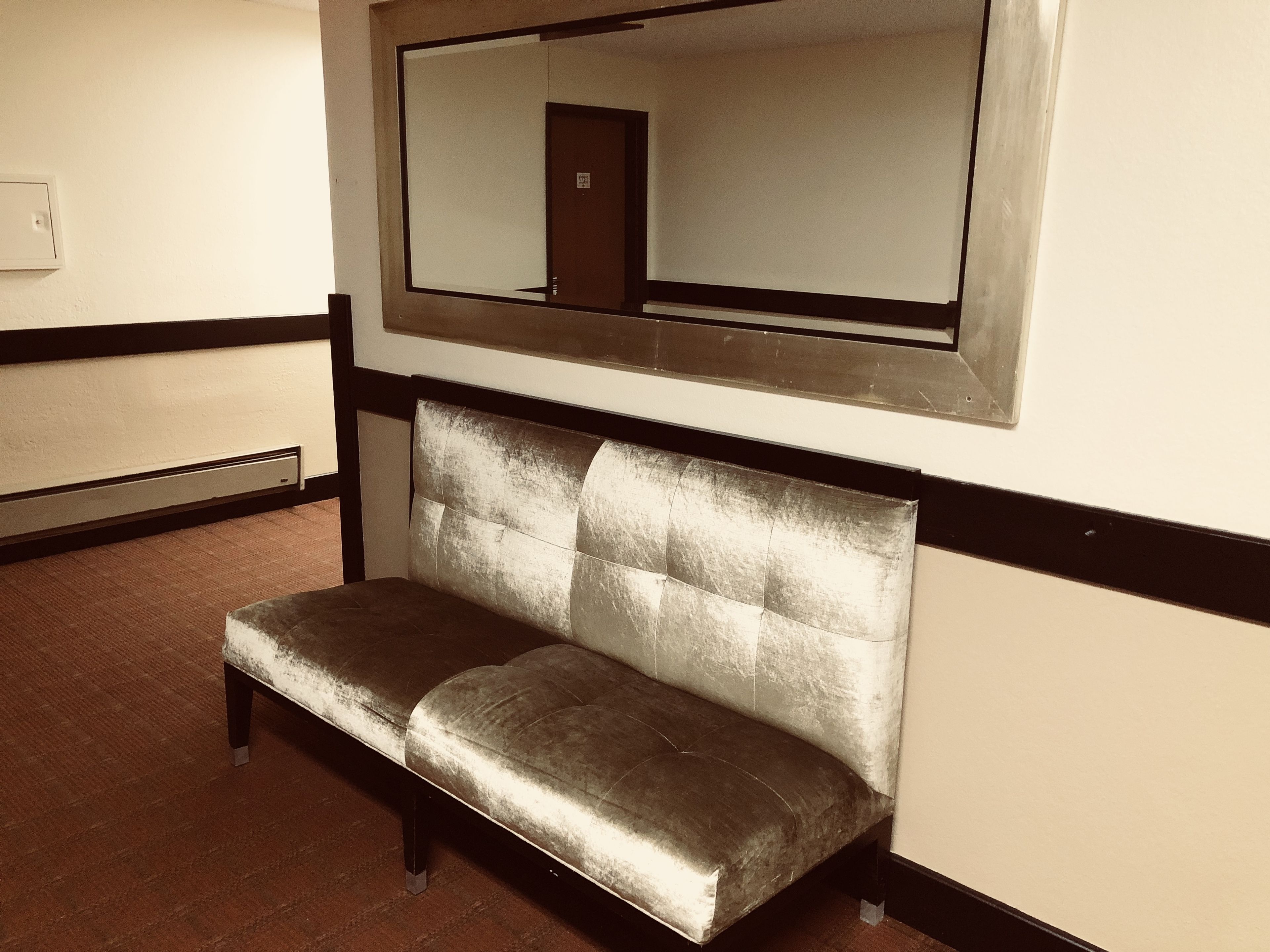 A bench with a cushioned backrest and metal legs, positioned against a wall with a large mirror above it.
