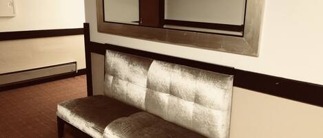 A bench with a cushioned backrest and metal legs, positioned against a wall with a large mirror above it.