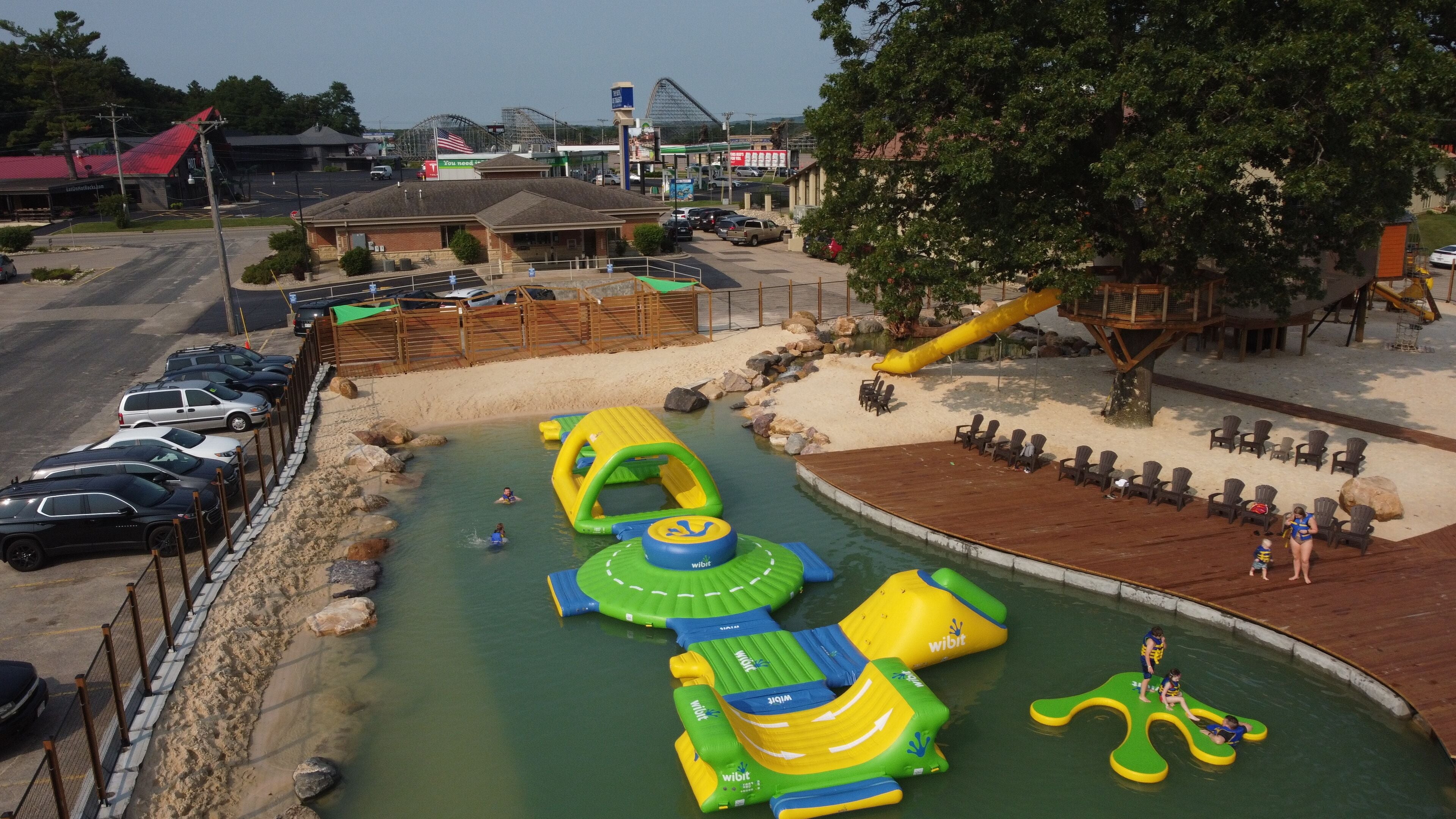 An outdoor swimming pool with inflatable water slides and a sandy area with lounge chairs.