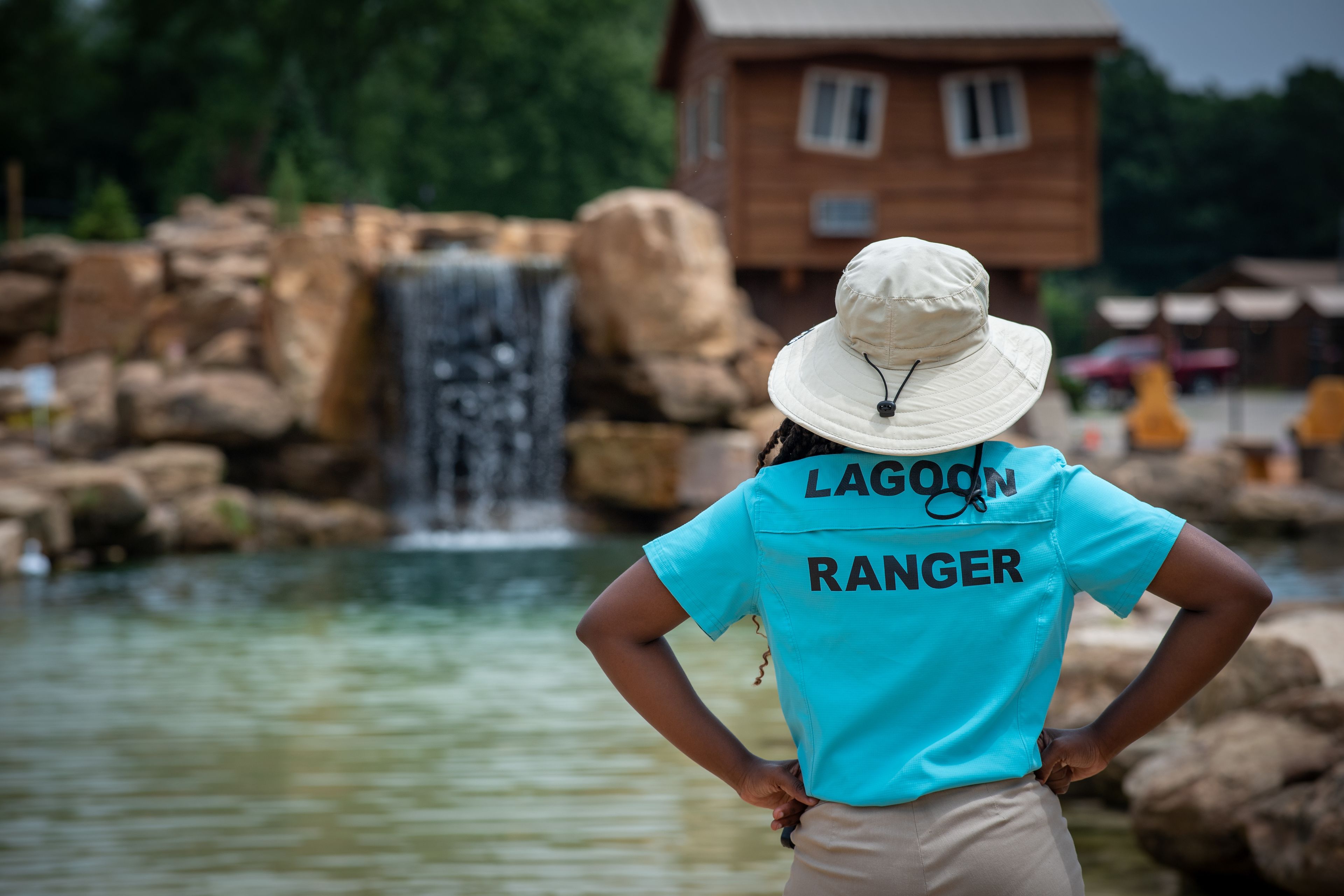 Une personne portant un t-shirt et un chapeau aux couleurs de « Lagoon Ranger », debout près d’une cascade.