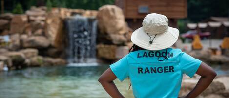 Une personne portant un t-shirt et un chapeau aux couleurs de « Lagoon Ranger », debout près d’une cascade.