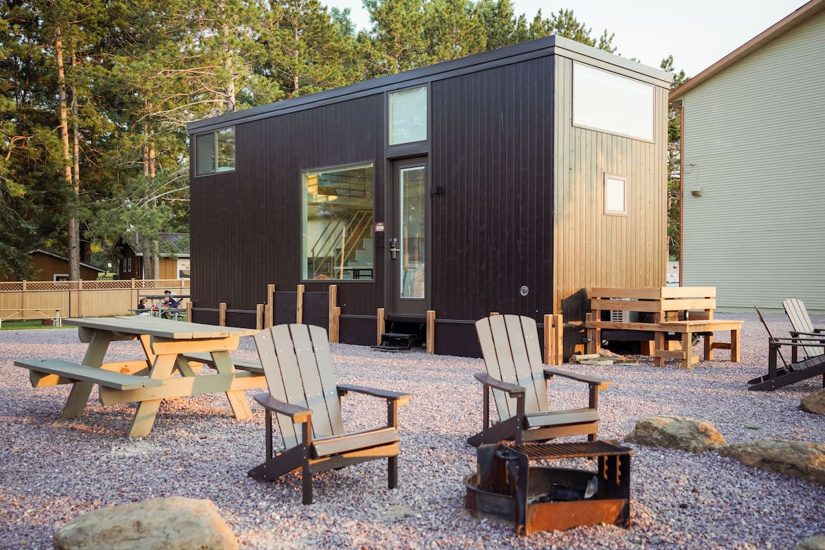 A modern cabin with a large deck area, outdoor seating, and a grill.