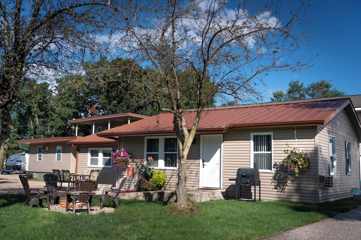 A two-story mobile home with a patio area, outdoor seating, and a hanging flower basket.