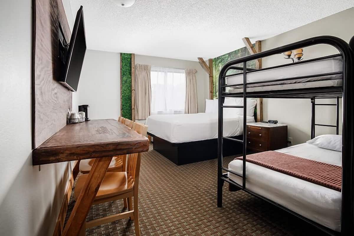 A hotel room with a bunk bed, a desk with a chair, a flat-screen TV mounted on the wall, and a window with curtains.