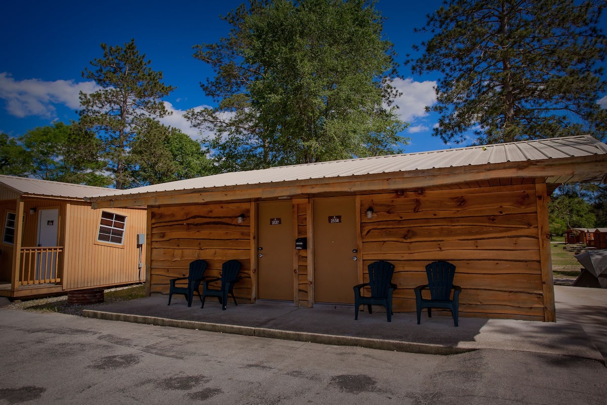 A log cabin with two doors, numbered 2537 and 2538, and two chairs outside.