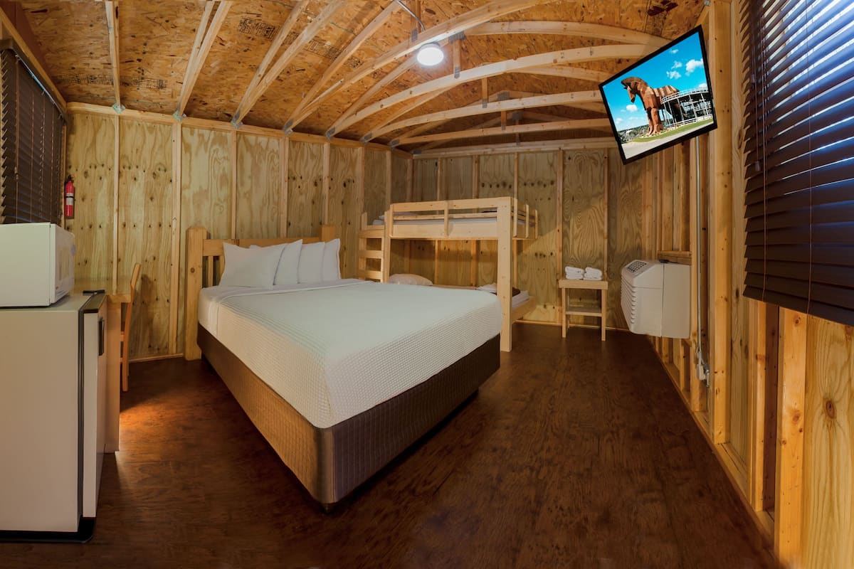 A wooden cabin room with a bunk bed, a small refrigerator, a television mounted on the wall, and a wooden ceiling.