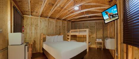 A wooden cabin room with a bunk bed, a small refrigerator, a television mounted on the wall, and a wooden ceiling.
