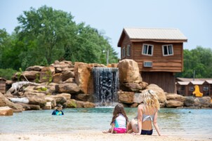 A wooden cabin with a metal roof, situated by a rocky waterfall.