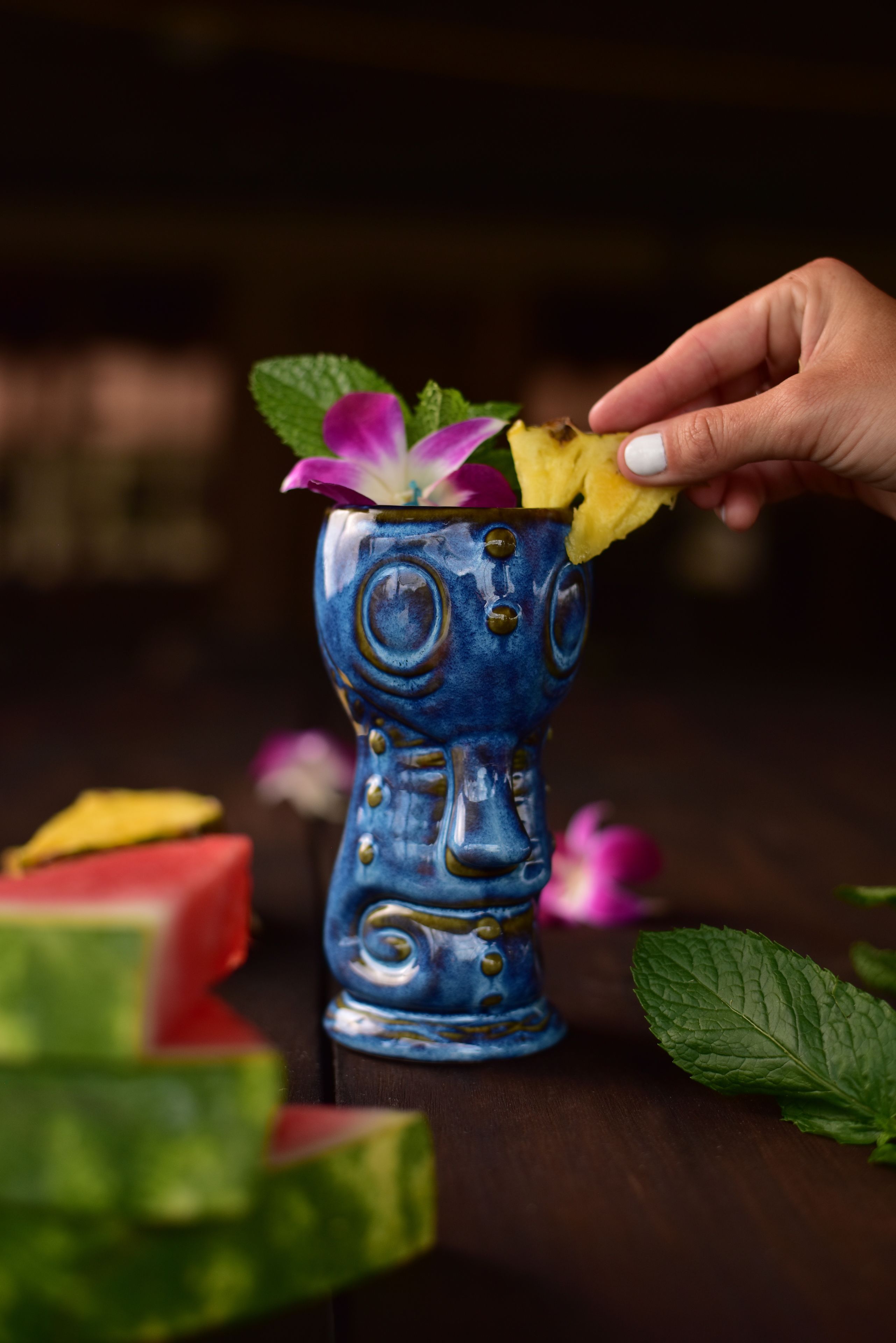 Uma mão colocando uma fatia de melancia em um vaso azul decorativo com um desenho floral.