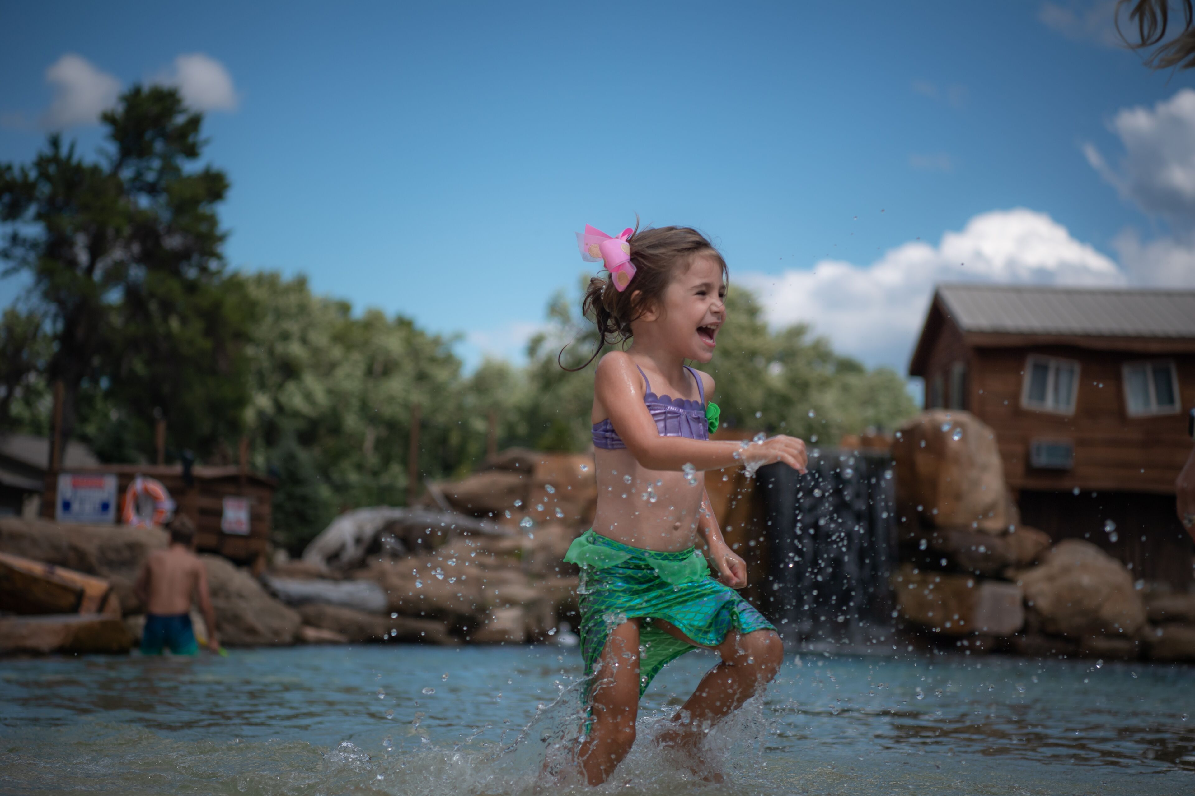 A child playing in a water feature with a waterfall, surrounded by rocks and trees.