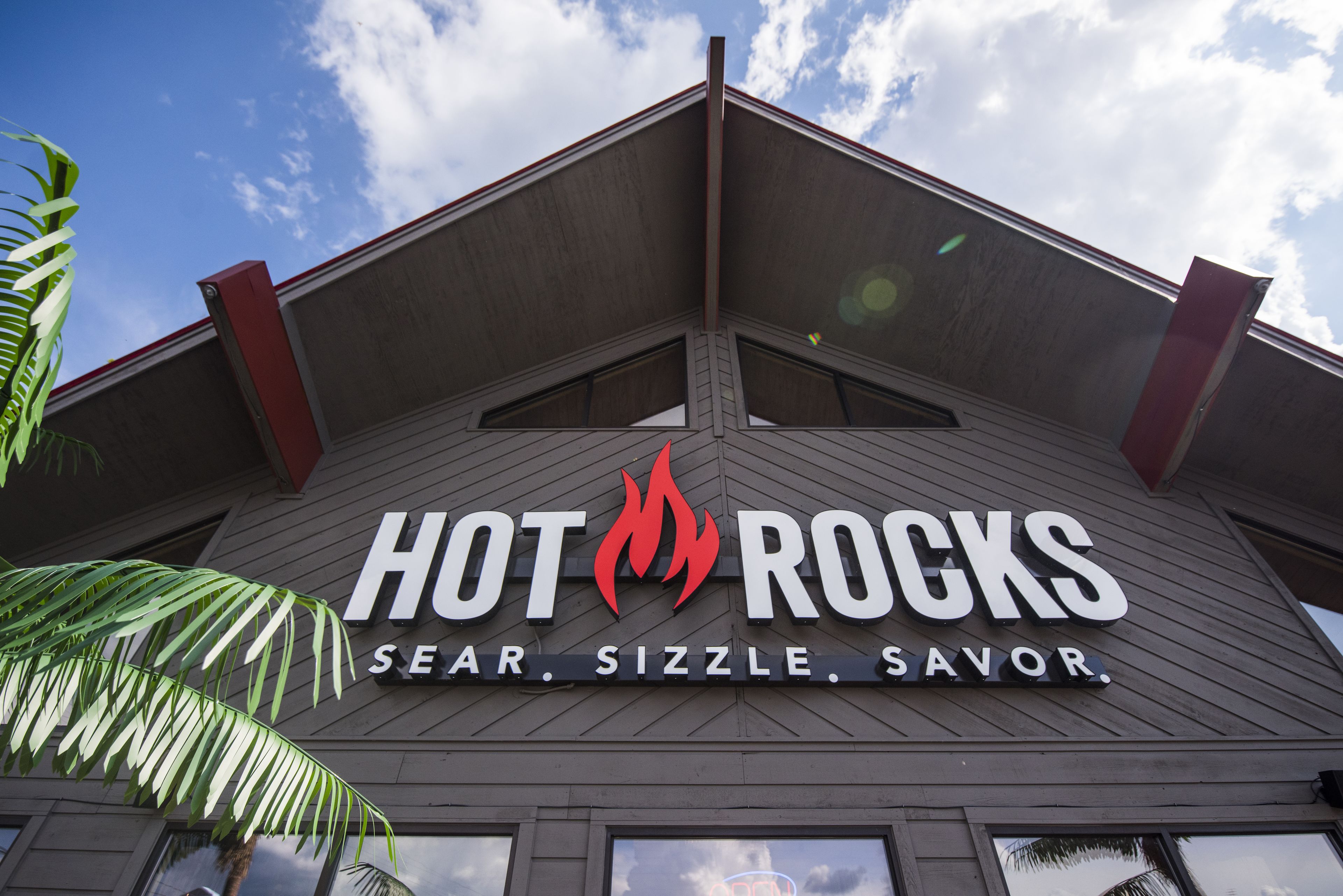 Un edificio con un letrero que dice “HOT ROCKS” y las palabras “SEAR. SIZZLE. SAVOR.”